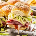 A spatula lifting a baked Italian slider with salami, cheese, and lettuce from a sheet pan.