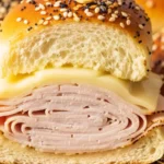 A close-up cross-section of a warm turkey and Swiss cheese slider on a buttery Hawaiian roll topped with everything bagel seasoning.