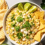 Overhead shot of a bowl of creamy Mexican Street Corn Dip garnished with lime and cilantro, served with tortilla chips.