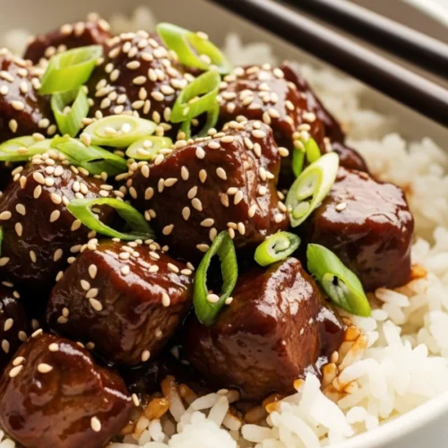 Close-up of tender beef cubes coated in a sticky soy glaze and toasted sesame seeds.
