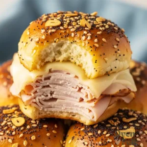 A close-up stack of turkey and melted Swiss cheese sliders on Hawaiian rolls topped with everything bagel seasoning.